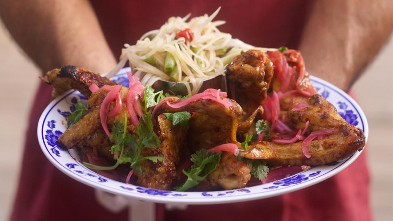 A person in a red apron serving Thai Bird jumbo chicken wings on a fancy blue and white plate
