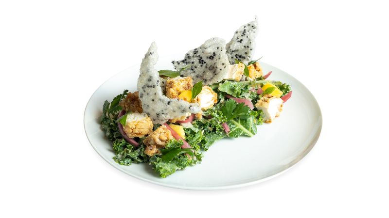 A plate of kale, ripe mango, crispy shallots, puffed rice crackers, and ginger dressing with your choice of chopped tender, rotisserie chicken or tofu.