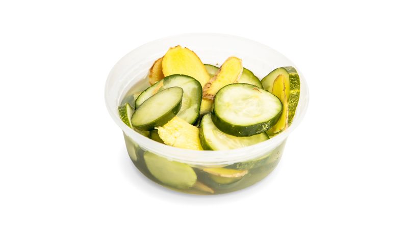 A cup of housemade pickles infused with fresh ginger slices.