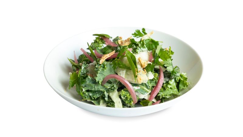 A bowl of fresh kale, pickled red onion, crispy shallots, and herbs tossed in ginger dressing.